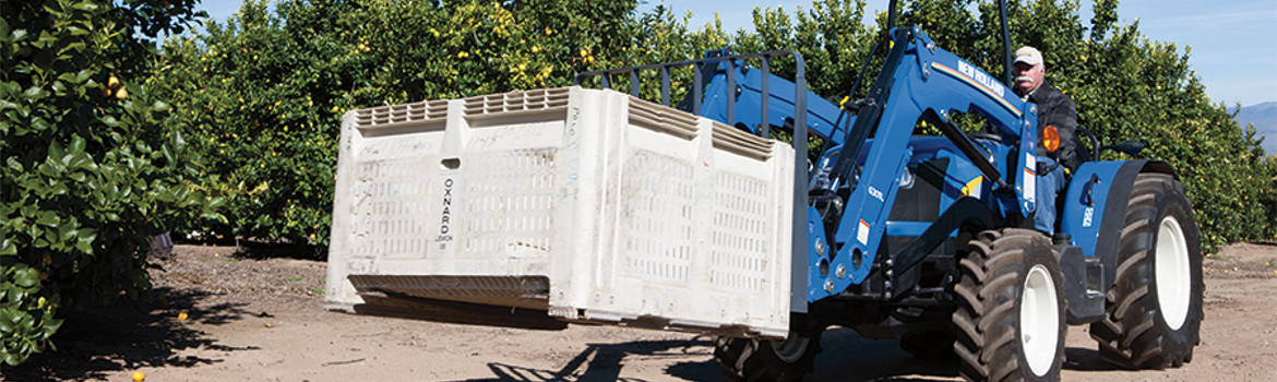 New Holland 600TL moving a crate of fruit in an orchard.